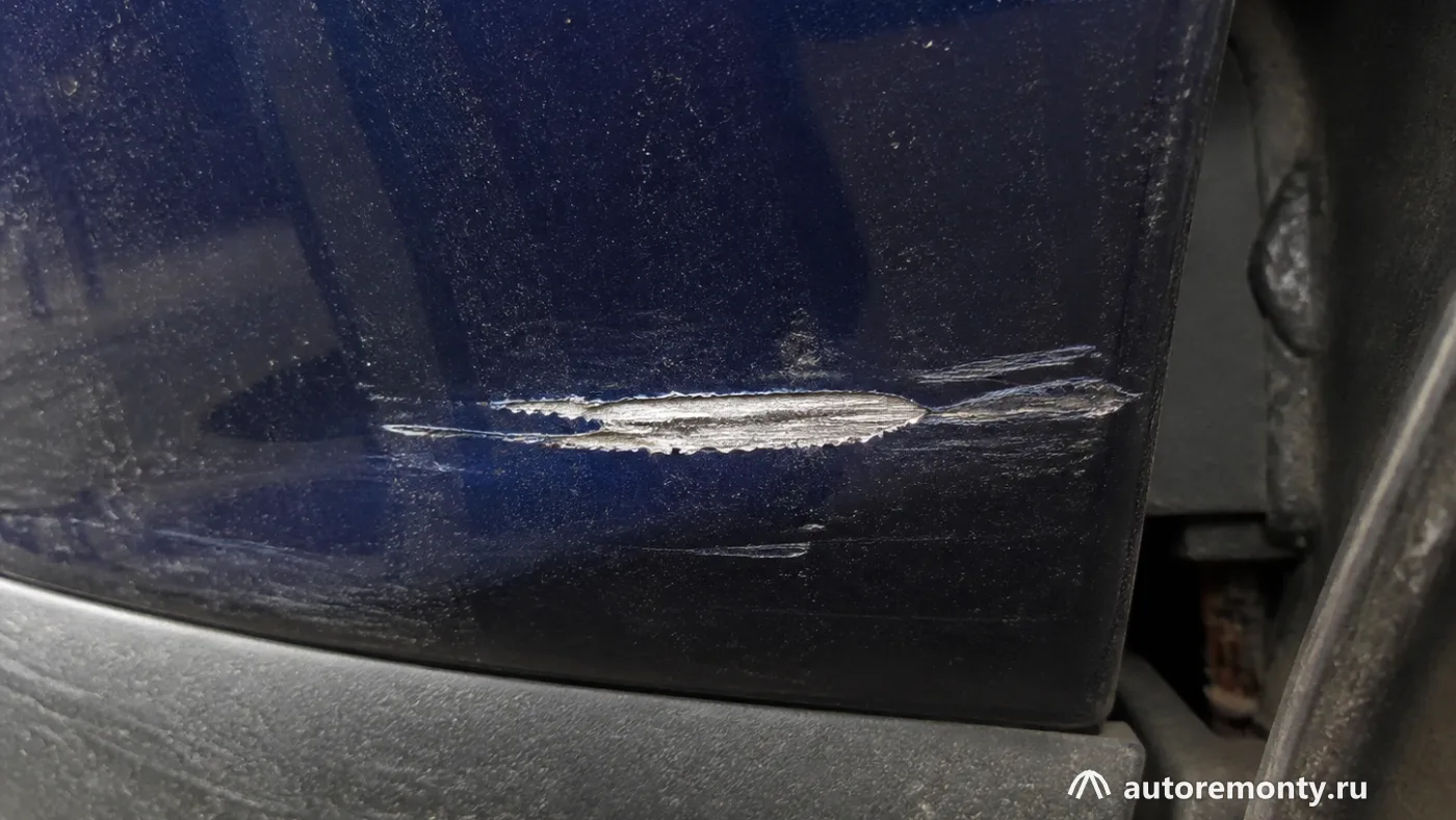 Глубокой царапины на окрашенной стальной кузовной панели, в центре видна узкая полоса чистого металла и — царапина до металла