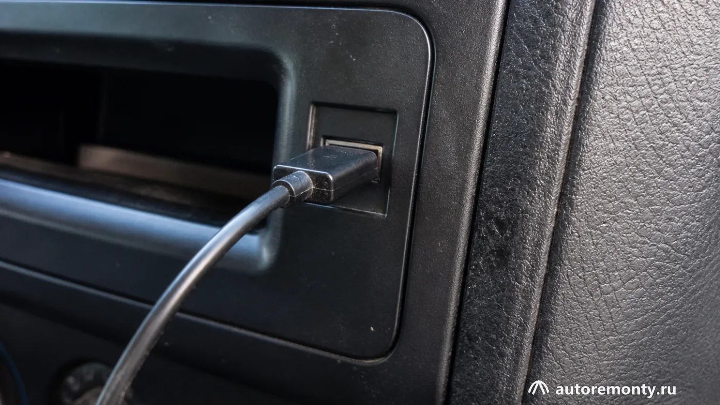 USB-порт мультимедийной системы и подключённый сертифицированный адаптер, с акцентом на разъём и кабель — машина без Apple CarPlay